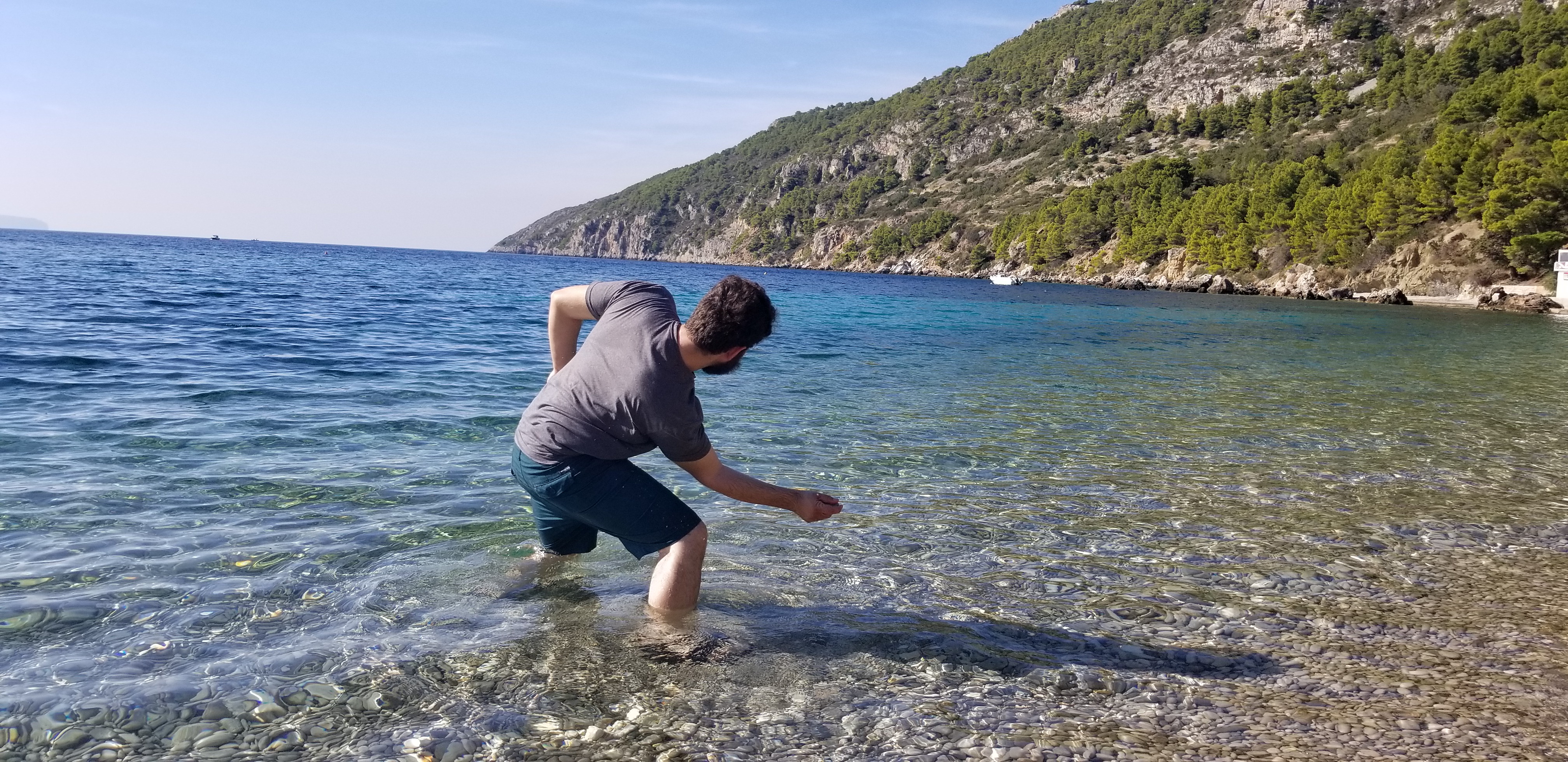 Josh stands in the water and slips rocks on a beach on the island of Hvar, Croatia